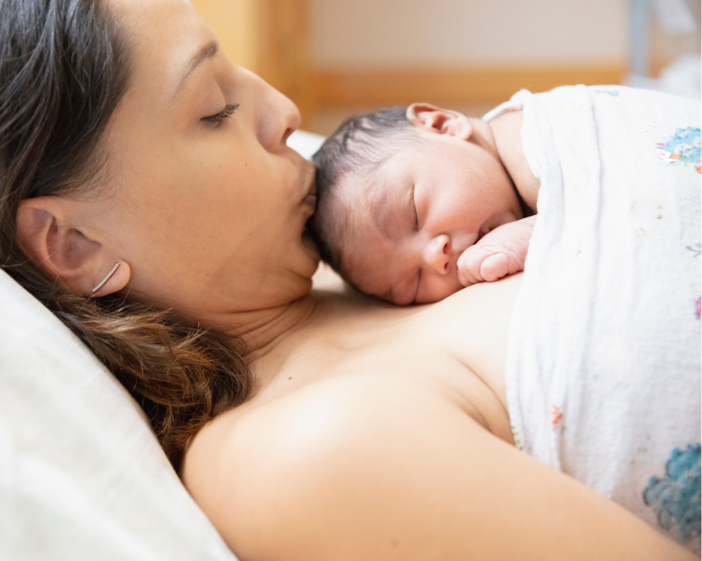 new mom kissing newborn baby on the head. The baby is lying on the mom's chest.