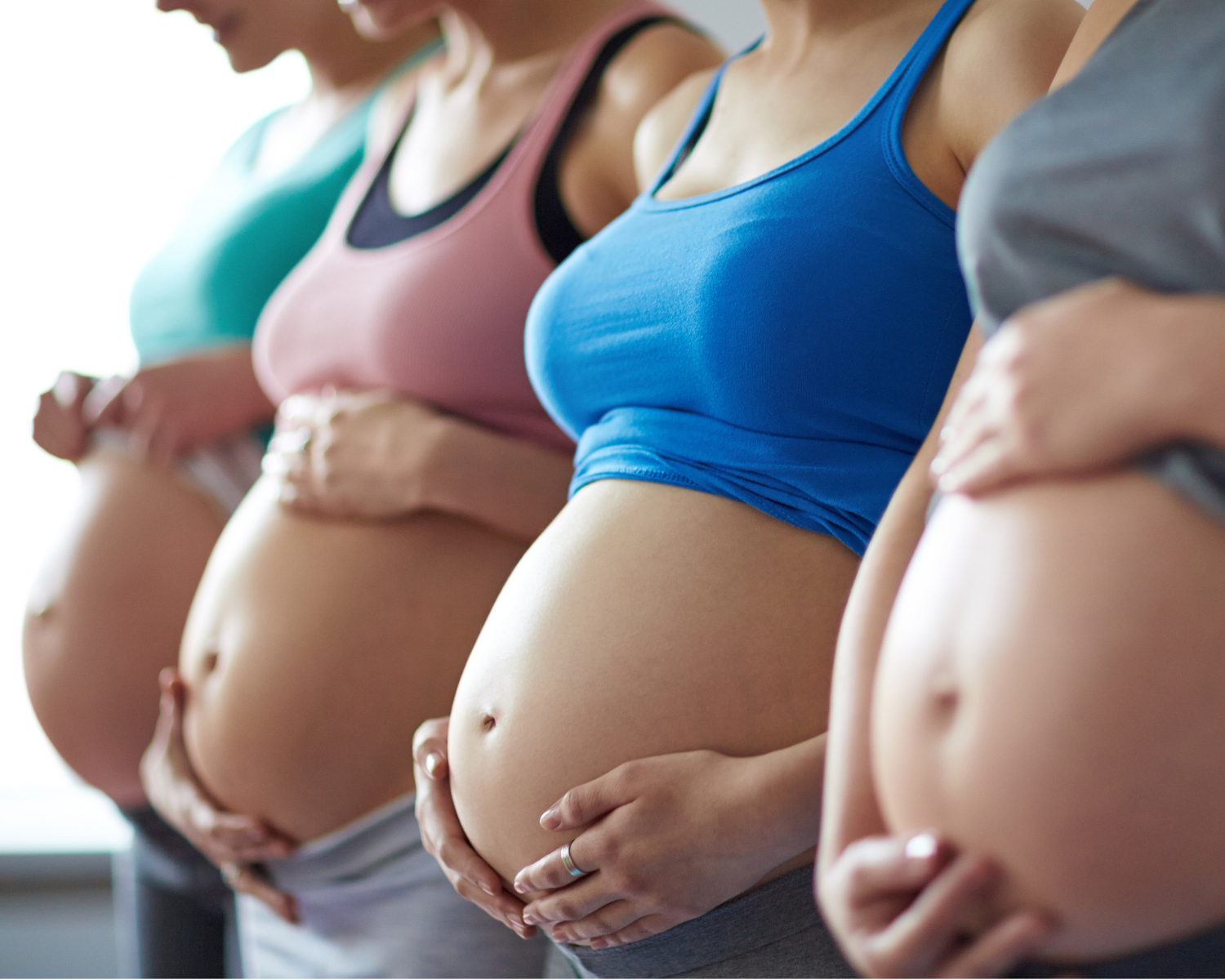 Photo of four pregnant women standing in a row with uncovered pregnant bellies