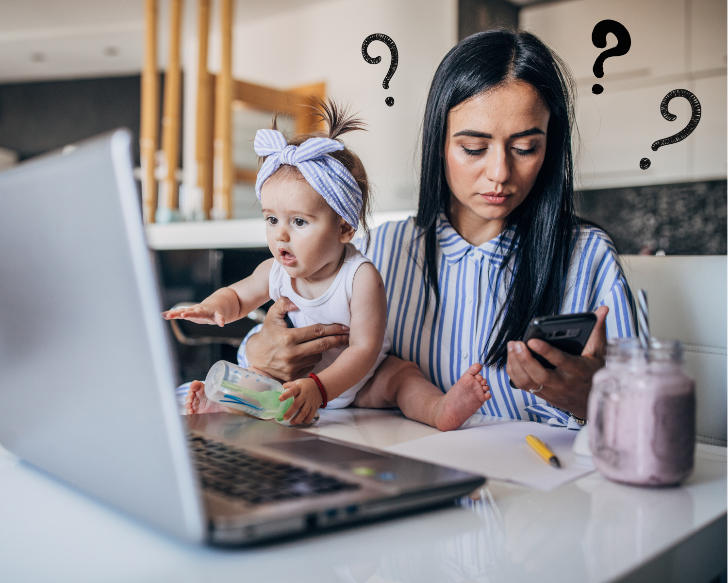 A mom and baby sitting at a table with a laptop open, a paper on the table, and mom is looking at her phone, confused.