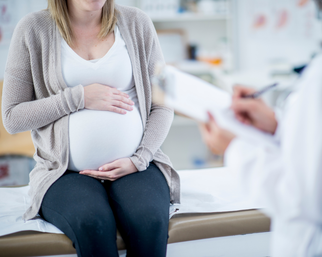 pregnant woman sitting on an exam table holding her belly in front of a health provider