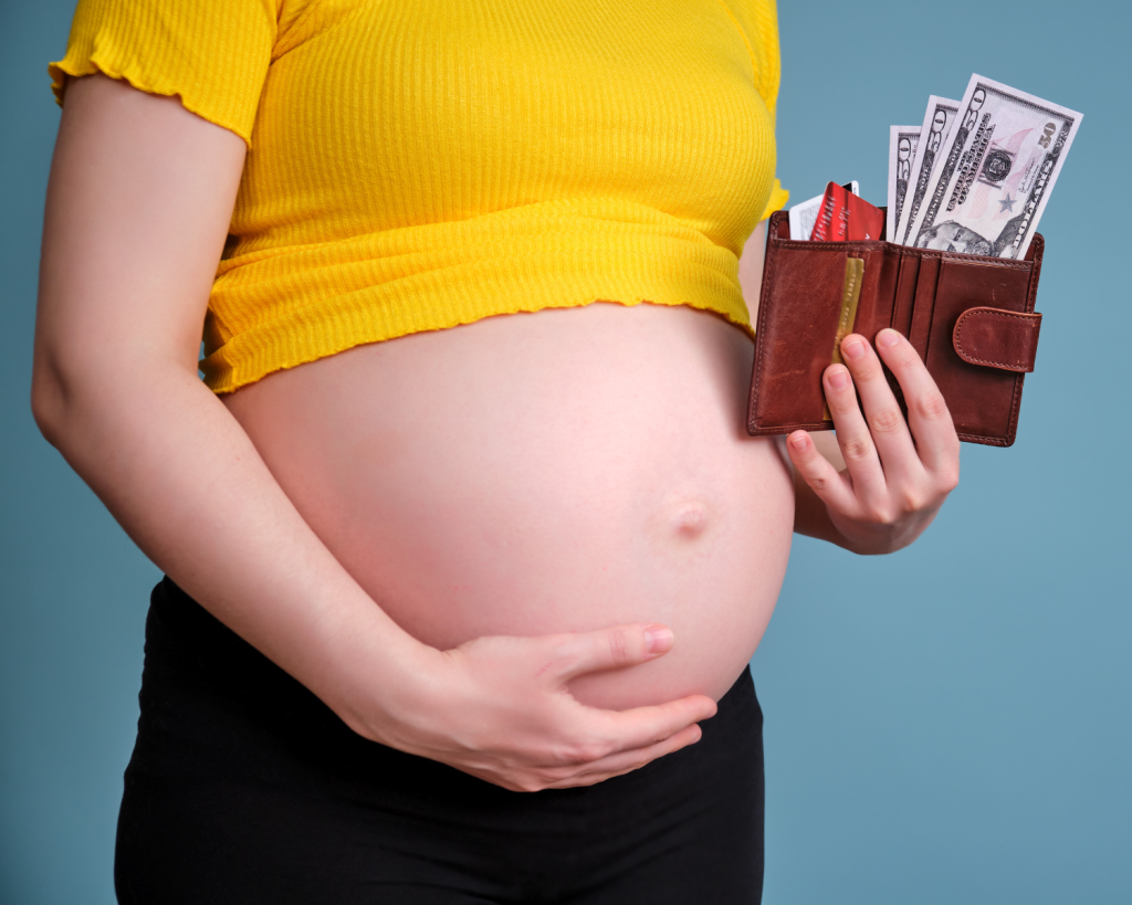 pregnant woman in a yellow shirt with belly exposed, holding her belly with one hand and her wallet with money hanging out in the other hand